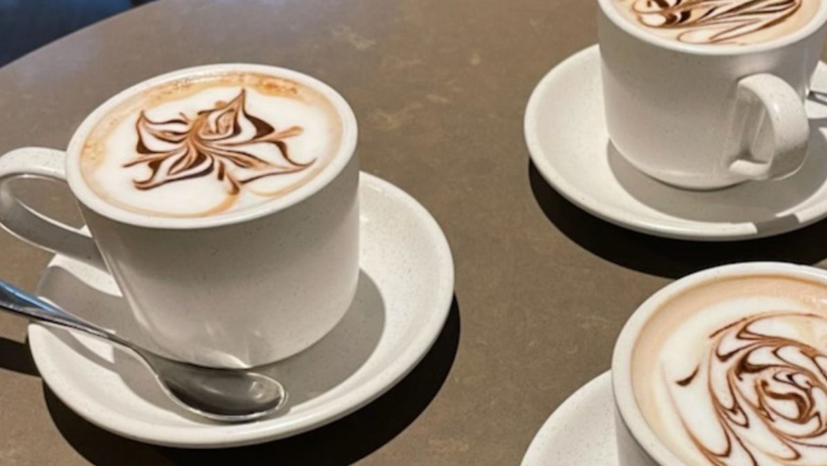 Close up of hotchocolates in white cup and sauce on table, the foam has "latte art" in chocolate on top.